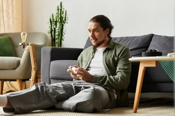 Handsome young man sits on the floor, focused on his gaming controller, enjoying leisure time. — Stock Photo