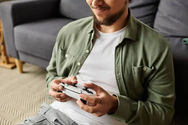 In a cozy living room, a young man engages in gaming, smiling as he plays with concentration. — Stock Photo