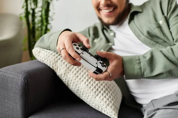 Young man smiles as he engages in gaming, surrounded by comfort and warmth at home. — Stock Photo