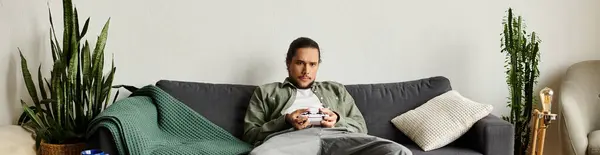 Bello giovane uomo si rilassa su un divano, profondamente concentrato su una console di gioco mentre a casa. — Foto stock
