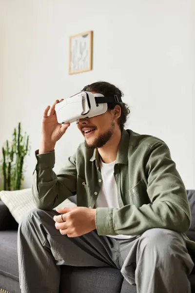 A handsome young man smiles while exploring virtual reality in his cozy living space, fully engaged. — Stock Photo