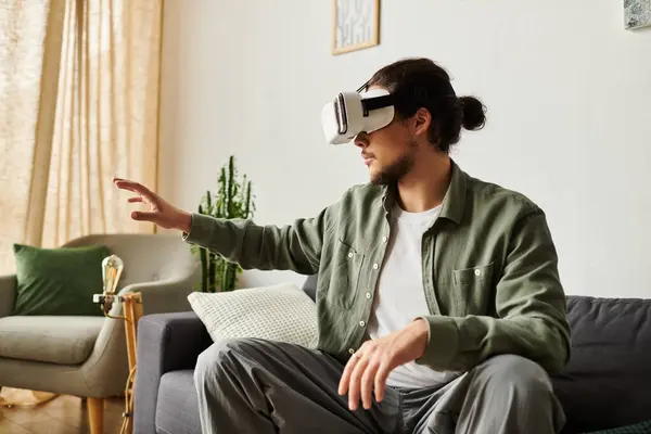 Un giovane bell'uomo si immerge nella realtà virtuale seduto su un comodo divano. — Foto stock