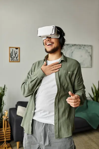 Joyful young man wearing a VR headset enjoys an immersive experience in his cozy living room. — Stock Photo