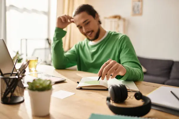A young, handsome man sits at a wooden table, focused on note taking while enjoying a drink. — Stock Photo