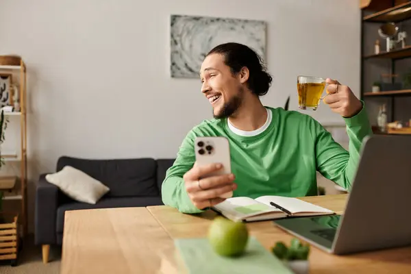 A handsome young man sips tea with a smile at a wooden table in a cozy home. — Stock Photo