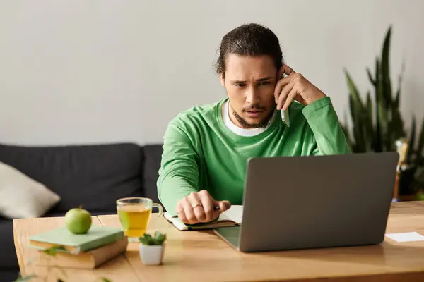 Focalizzato giovane uomo parla al telefono e tipi note mentre seduto a un tavolo di legno. — Foto stock