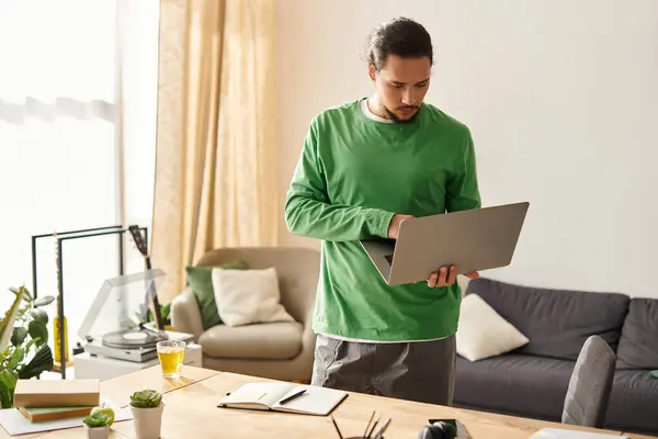 A young handsome man stands in a well lit room, focused on his laptop, surrounded by home decor. — Stock Photo