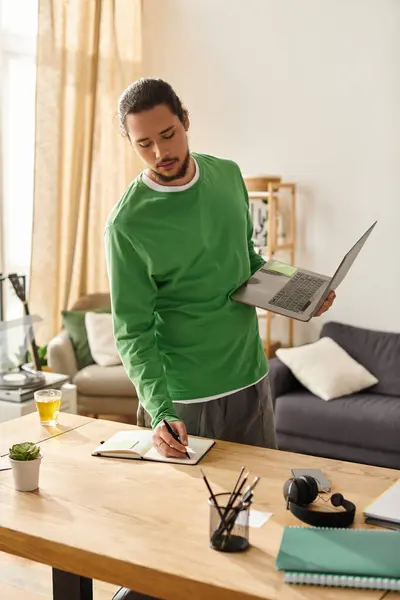 Smartly dressed in green, the young man writes notes as he balances a laptop in his hand. — Stock Photo