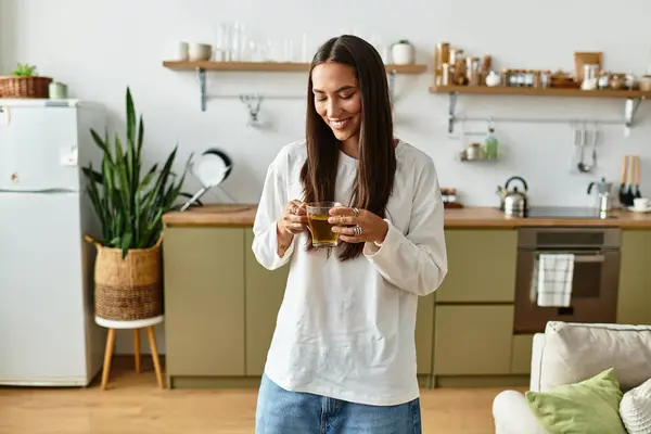 Luminosa e invitante atmosfera come una giovane donna sorseggia il suo drink, sorridendo nella sua cucina accogliente. — Foto stock