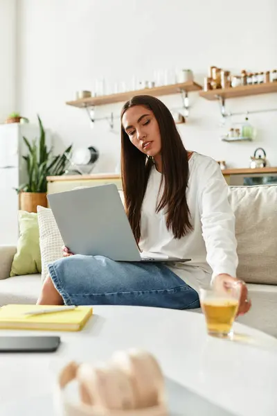 Young woman engages with her laptop at home while sipping a drink in a cozy atmosphere. — Stock Photo