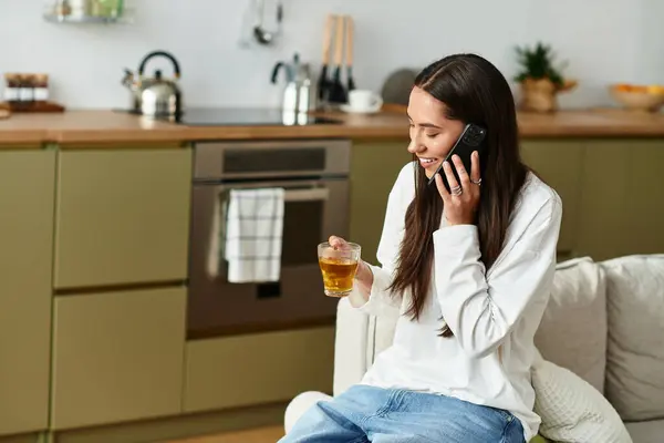 Une jeune femme se détend à la maison, sirotant un verre et bavardant au téléphone. — Photo de stock