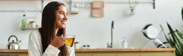 A young, beautiful woman relaxes at home, savoring a cup of tea with a joyful smile. — Stock Photo