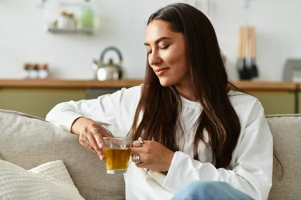 Beautiful young woman savors a warm drink, surrounded by a comfy, inviting home atmosphere. — Stock Photo