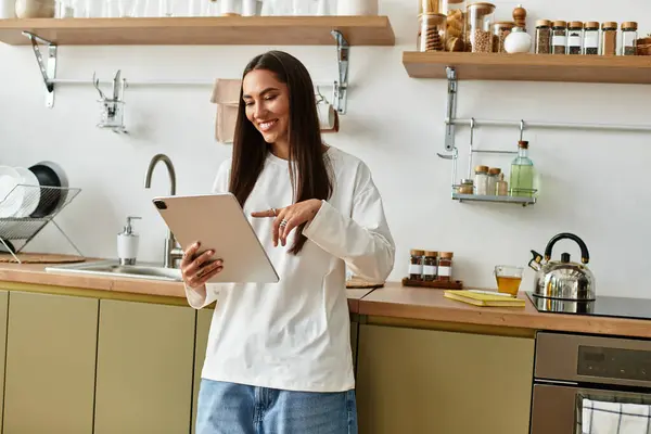 Bright and cozy kitchen moments captured as a young woman engages with her tablet, smiling. — Stock Photo