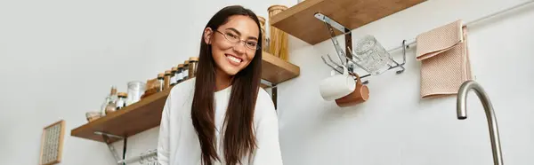 Hermosa mujer joven sonríe mientras prepara la comida en su espacio de cocina brillante y cálido. - foto de stock