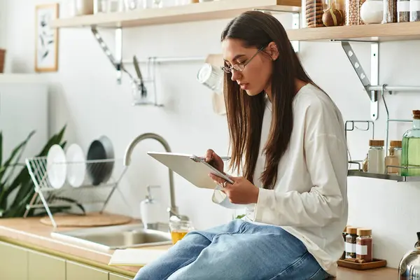 Pretty woman relaxes at home, deeply focused on her tablet while seated in a cozy kitchen. — Stock Photo