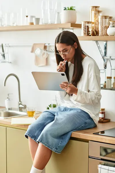 A young woman relaxes at home on the kitchen counter, using her tablet. — Stock Photo