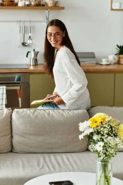 Bright and cozy atmosphere fills the space as a young woman writes in her notebook, smiling happily. — Stock Photo