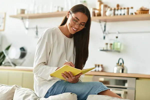 A young woman smiles, writing in her notebook at home in the cozy morning light. — Stock Photo