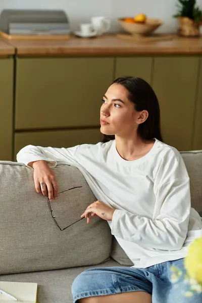 A young woman sits comfortably on her couch, reflecting and enjoying her peaceful day at home. — Stock Photo
