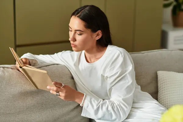 A young woman relaxes on a couch, absorbed in her book on a quiet afternoon. — Stock Photo