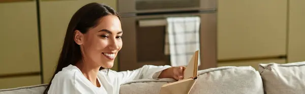 Una giovane donna sorride con un libro, creando un'atmosfera calda nella sua accogliente casa. — Foto stock