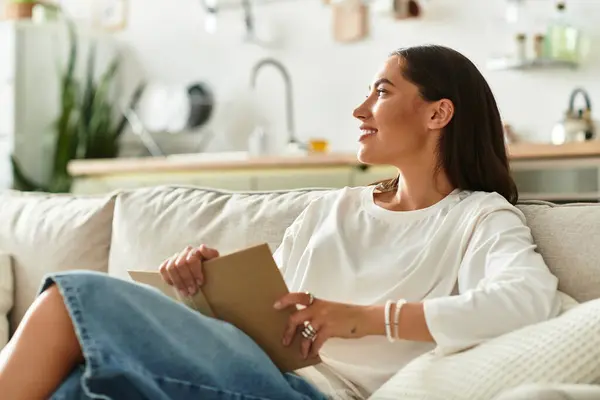 Relaxing at home, a young and beautiful woman enjoys reading while sitting comfortably. — Stock Photo
