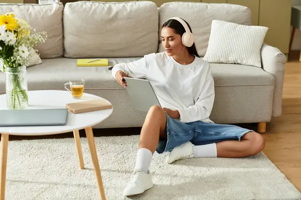 Young woman sits comfortably on the floor, focused on her tablet while listening to music. — Stock Photo