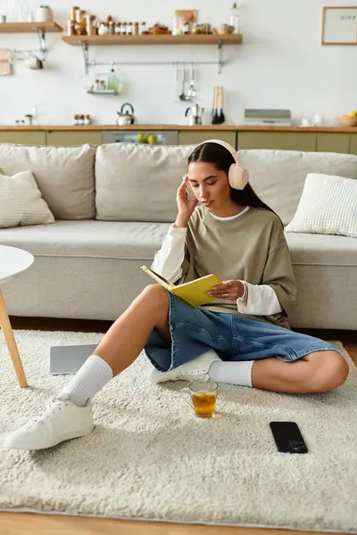 Beautiful woman relaxes at home with her book, sipping tea and enjoying music on a comfy day. — Stock Photo