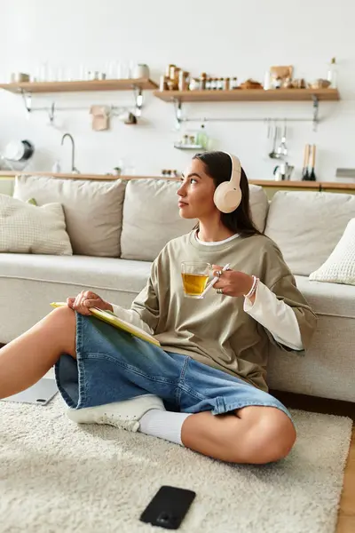 Beautiful woman relaxes on the floor at home, sipping tea and capturing thoughts in a journal. — Stock Photo
