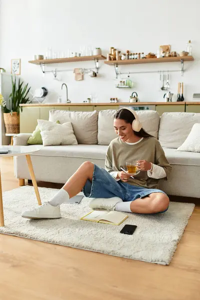 Eine junge Frau genießt ihre Zeit zu Hause und schlürft Tee, während sie es sich in kuscheliger Kleidung gemütlich macht. — Stockfoto