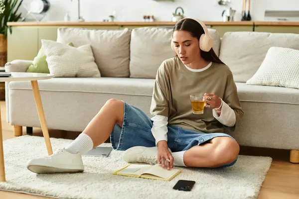 Zu Hause sitzt eine schöne junge Frau gemütlich mit einem Buch und Tee auf dem Fußboden. — Stockfoto