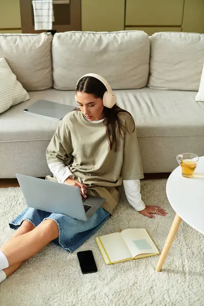 A young woman sits on the floor with her laptop and notes, enjoying a serene moment at home. — Stock Photo