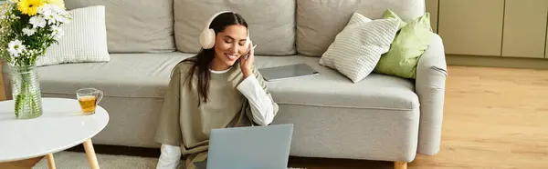 Young woman sits comfortably at home, focused on her laptop while enjoying a warm drink. — Stock Photo