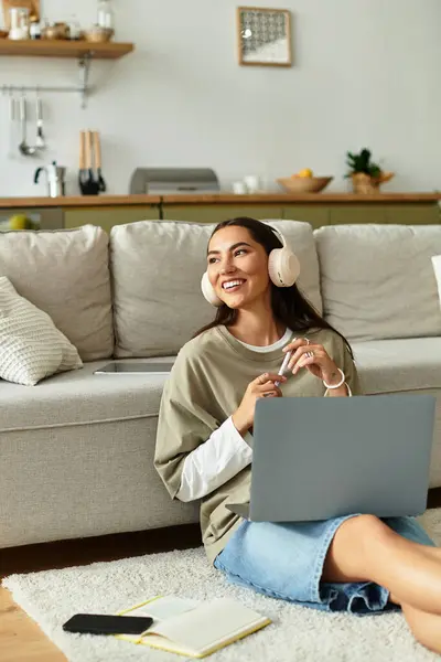 Eine fröhliche junge Frau lächelt, während sie mit ihrem Laptop in einem gemütlichen Wohnzimmer auf dem Boden sitzt. — Stockfoto