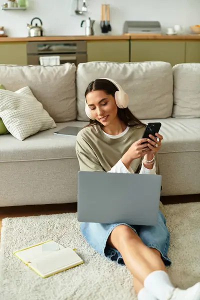 Relaxing comfortably at home, a young woman balances her smartphone and laptop, smiling. — Stock Photo
