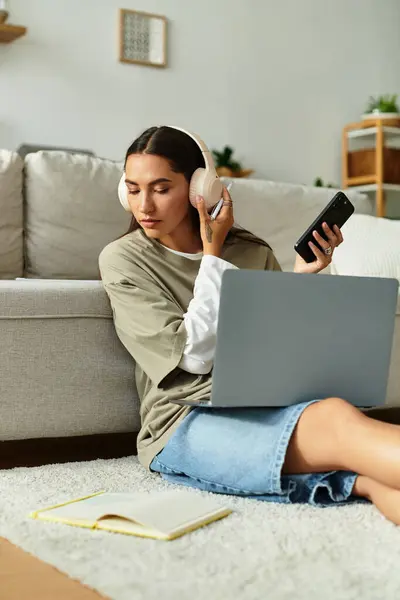 A pretty young woman sits on the floor, focused on her laptop, listening to music, and taking notes. — Stock Photo
