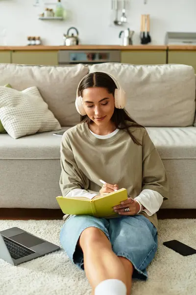 Una joven escribe en su diario en el suelo, acogedora y escuchando música. - foto de stock