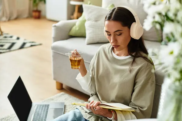 Relajándose en casa, una joven escucha música mientras disfruta del té y lee notas. — Stock Photo
