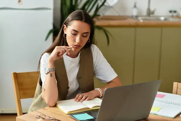 A pretty young woman sits thoughtfully at her dining table, engaged in her studies at home. — Stock Photo