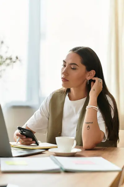 A beautiful young woman sits comfortably at home, focused on her smartphone while sipping coffee. — Stock Photo