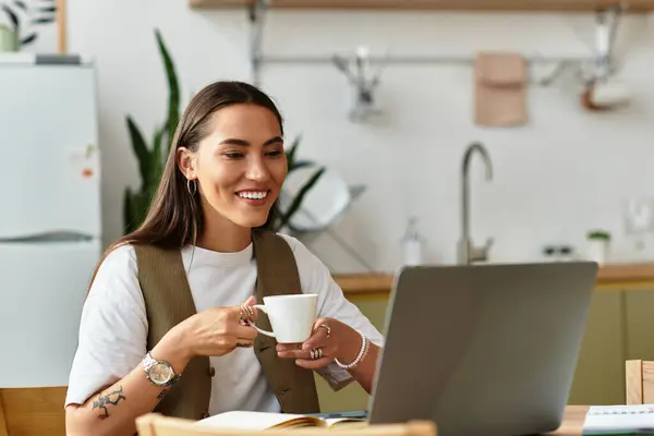A young woman delights in her time at home, sipping a warm drink while focused on her laptop. — Stock Photo