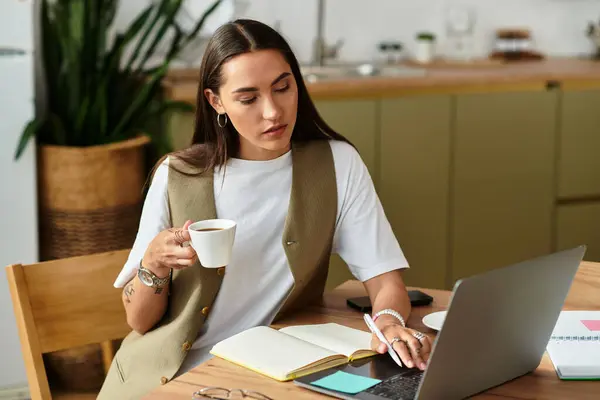 A young woman sits comfortably at her kitchen table, sipping coffee and focused on her work. — Stock Photo