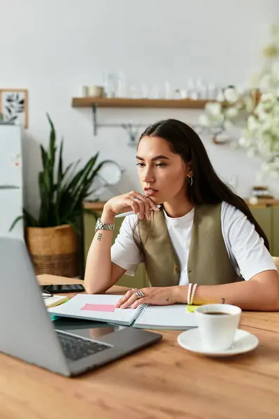 A beautiful young woman sits comfortably at her desk, focused on her laptop and enjoying coffee. — Stock Photo
