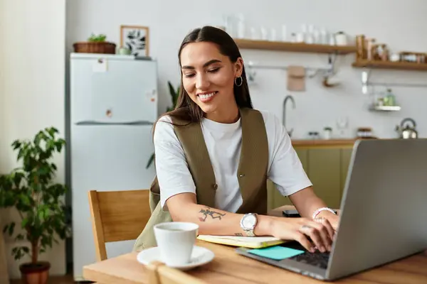 Beautiful woman smiles while working on laptop, sipping coffee in a bright and cozy kitchen. — Stock Photo