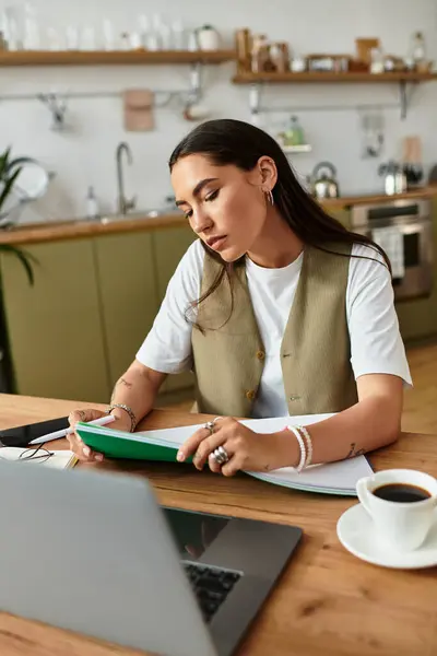 Una mujer bonita se sienta cómodamente en casa, centrándose en sus estudios mientras disfruta del café. - foto de stock