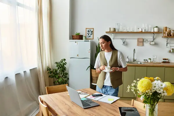 Pretty woman sits at her kitchen table with a warm drink, balancing work and comfort at home — Stock Photo