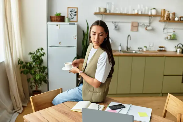 A beautiful woman relaxes in her comfy kitchen, sipping coffee and engaging with her laptop. — Stock Photo