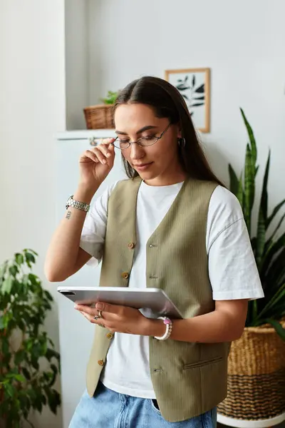 Beautiful young woman engages with a tablet, surrounded by green plants in her cozy home. — Stock Photo