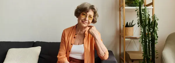 Mature woman dressed in comfy clothes sits on a couch, radiating warmth and happiness at home. — Stock Photo